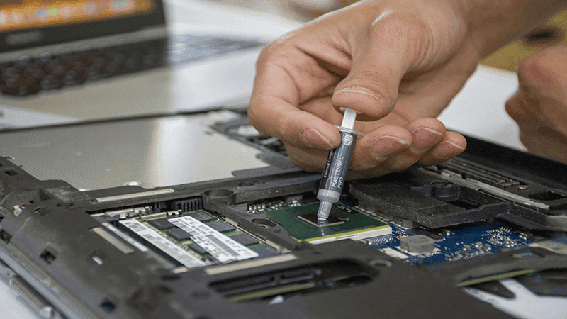 Person applying thermal paste onto a CPU chip on a laptop motherboard.