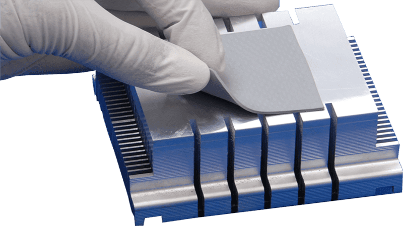 Thermal pad installation: Gloved hand placing a gray thermal pad onto a silver aluminum heat sink, designed for heat dissipation in electronic components (CPU, GPU) in computing or industrial electronics