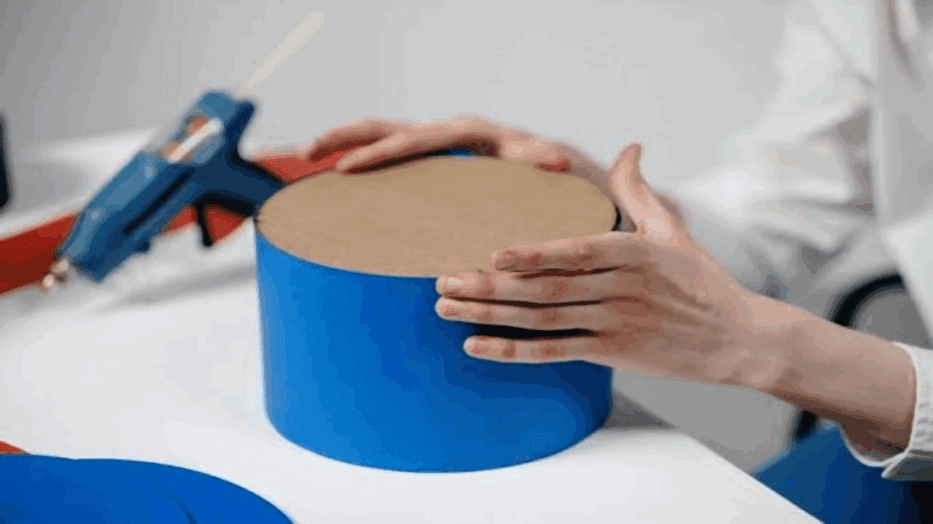 A person is using a glue gun to make a blue box.