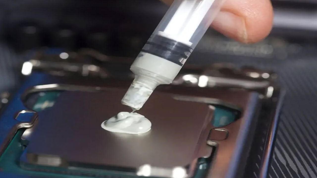 A close-up shot of a hand applying a pea-sized amount of thermal paste from a syringe onto a CPU.