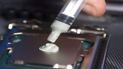 A close-up shot of a hand applying a pea-sized amount of thermal paste from a syringe onto a CPU.